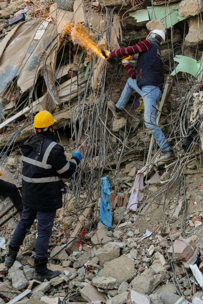 Rescue workers wearing helmets cut through rubble in a city disaster scene, working on recovery efforts.